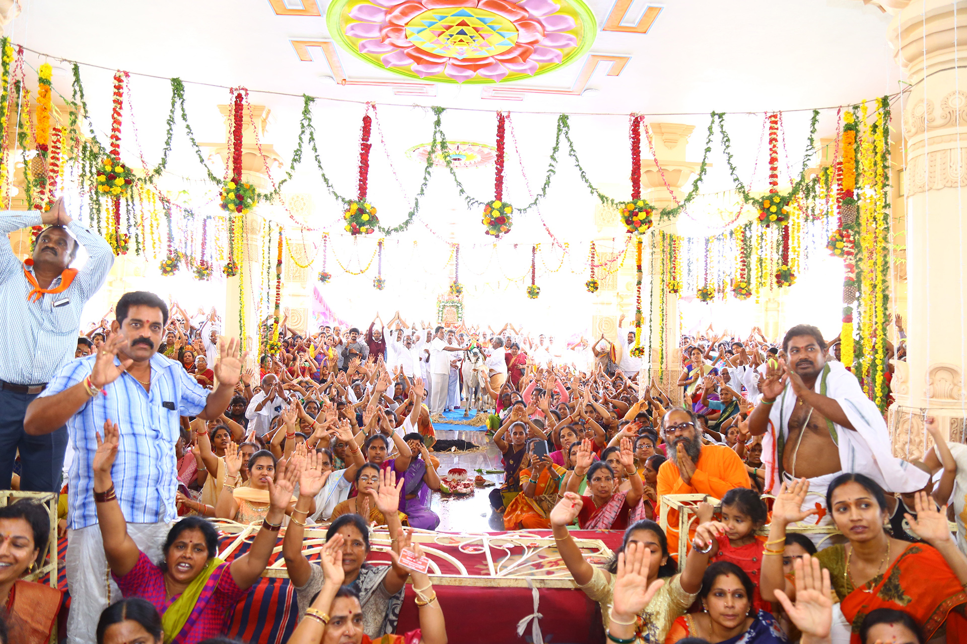 crowd of people in colorful outfits and building decorated in flowers raising their hands