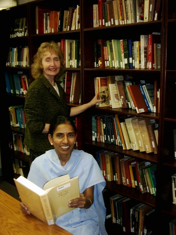 woman reading a book at a library and woman selecting a book behind her