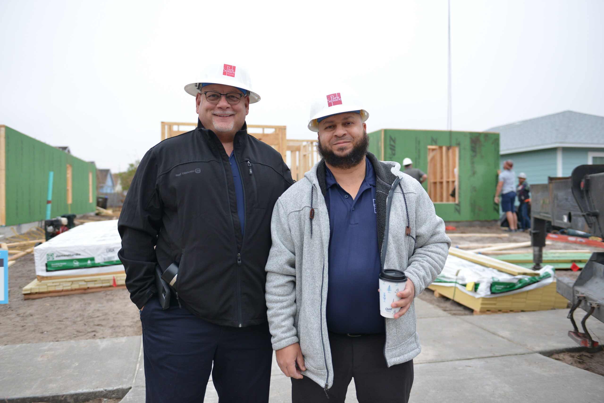 two Park Square Homes members standing in construction hats outside of a house being built