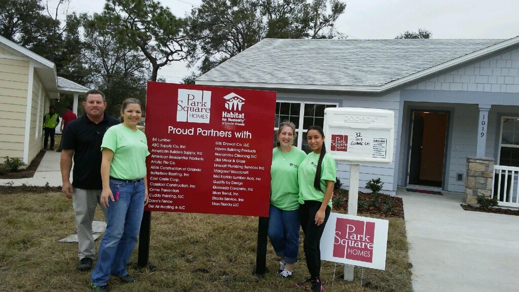 Workers pose by a sign in between houses Park Square Homes and Habitat for Humanity partners