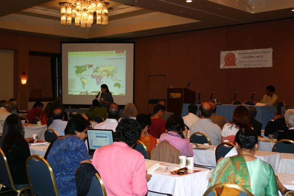 people sit at tables listening to a speaker at The Hindu University of America event