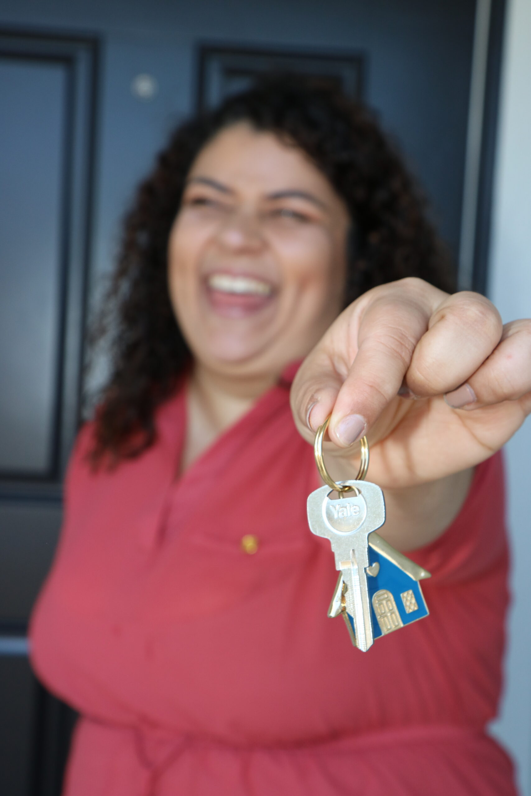 woman smiling and holding up a set of keys in front of a house door