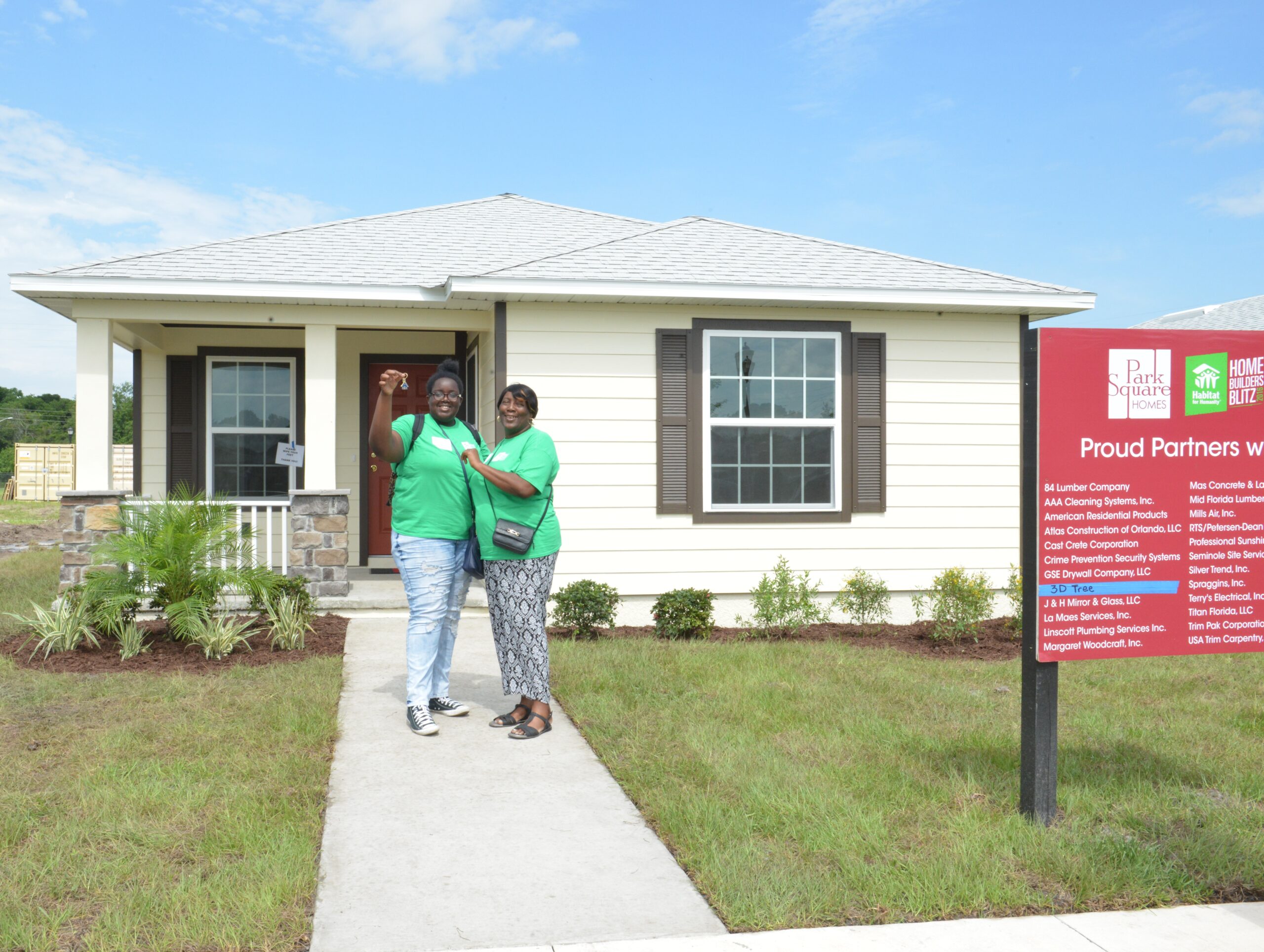 new homeowners hold up a key smiling on front sidewalk