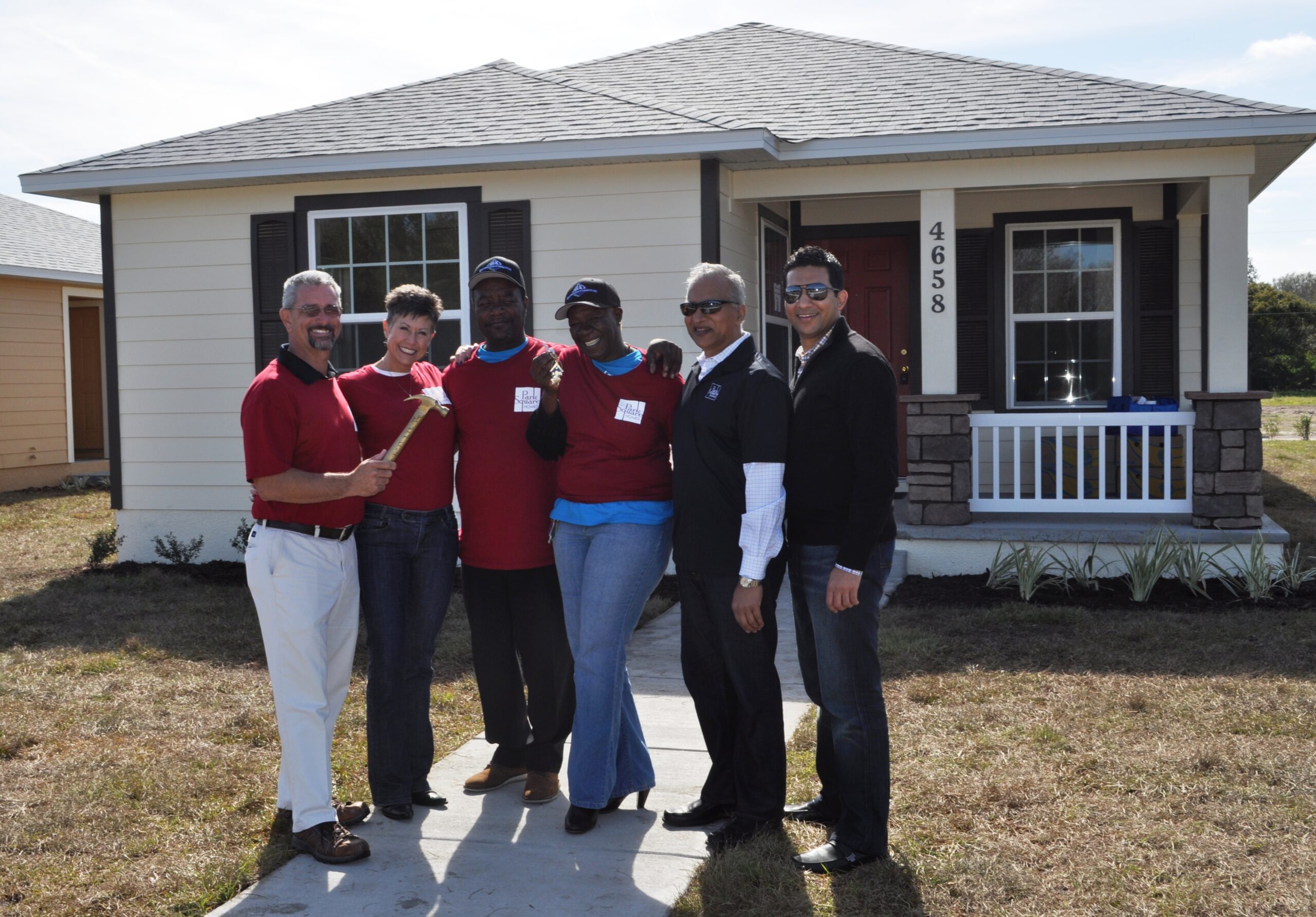 new homeowner and Park Square Homes team poses outside of a new house with golden hammer