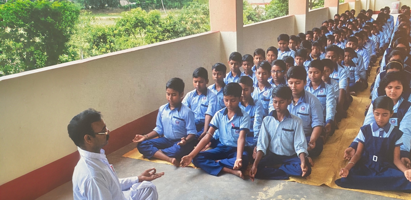 children sitting in rows meditating with a teacher in rural India